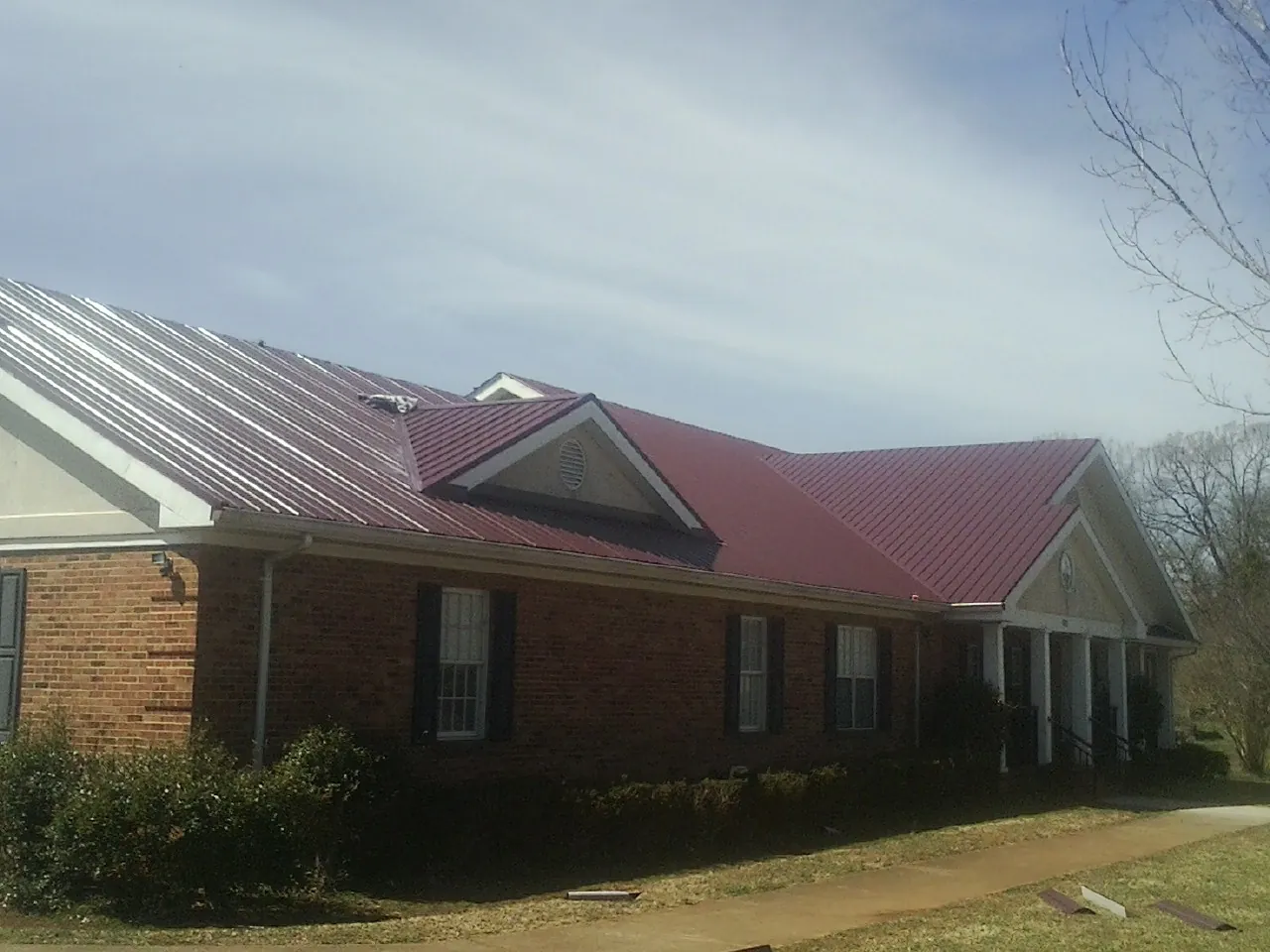 Red metal roof with gabled entries on a long brick building, from a Hail Damage Roof Repair job in Brockton