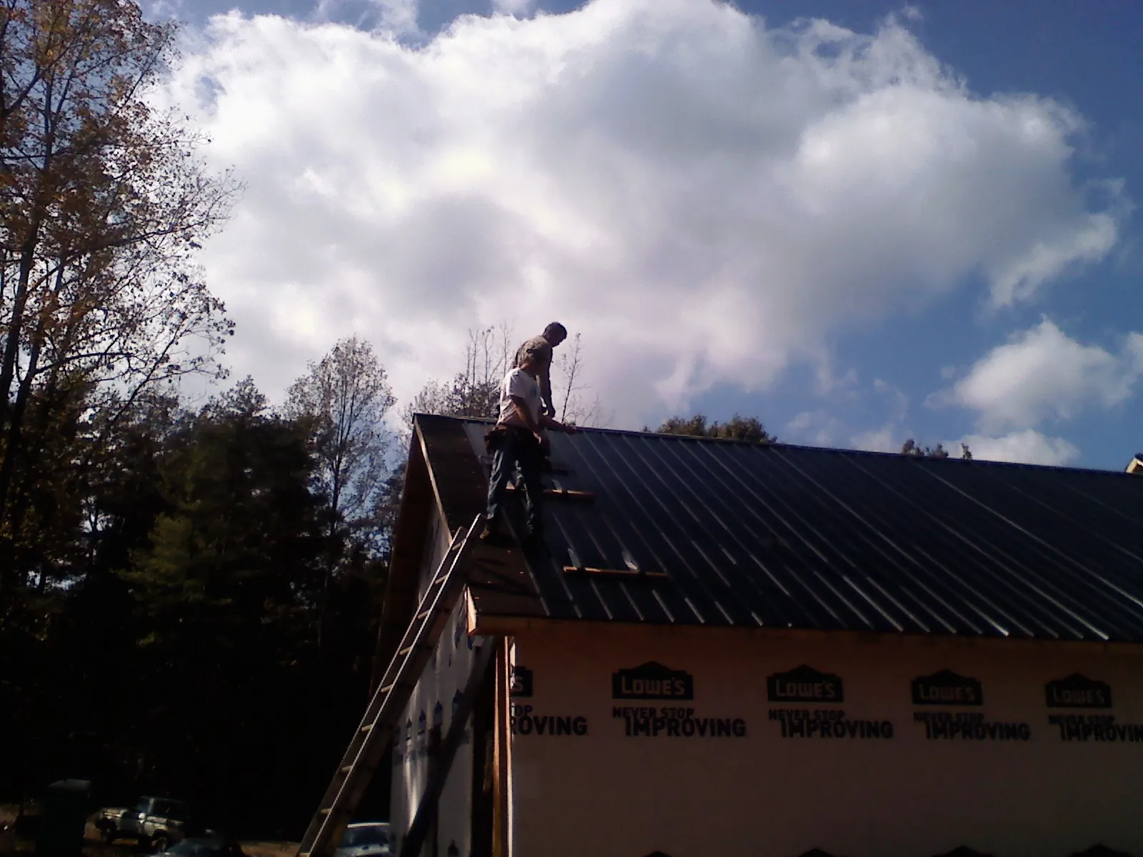 Roofer fastening dark metal panels high against a cloudy sky, from a Roof Inspection job in Brockton