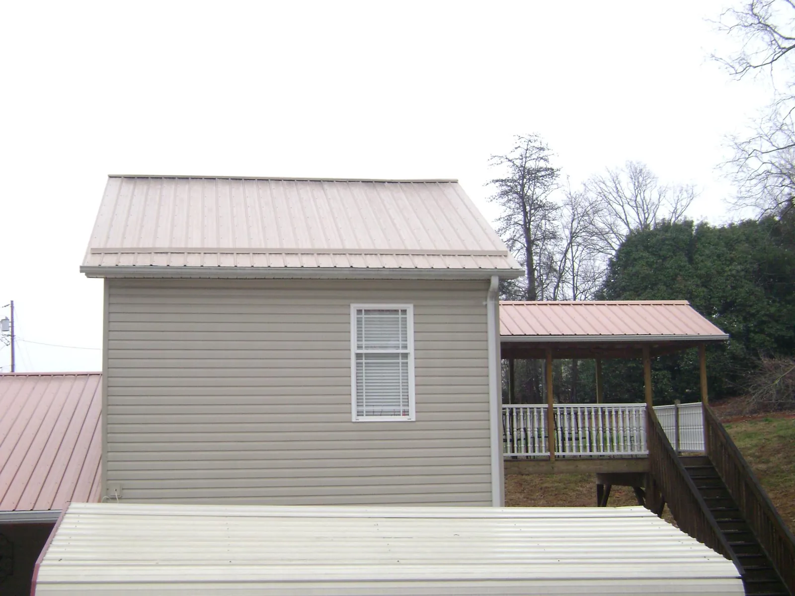 Tan metal roofs on a two story addition and attached porch, from a Roof Replacement job in Brockton